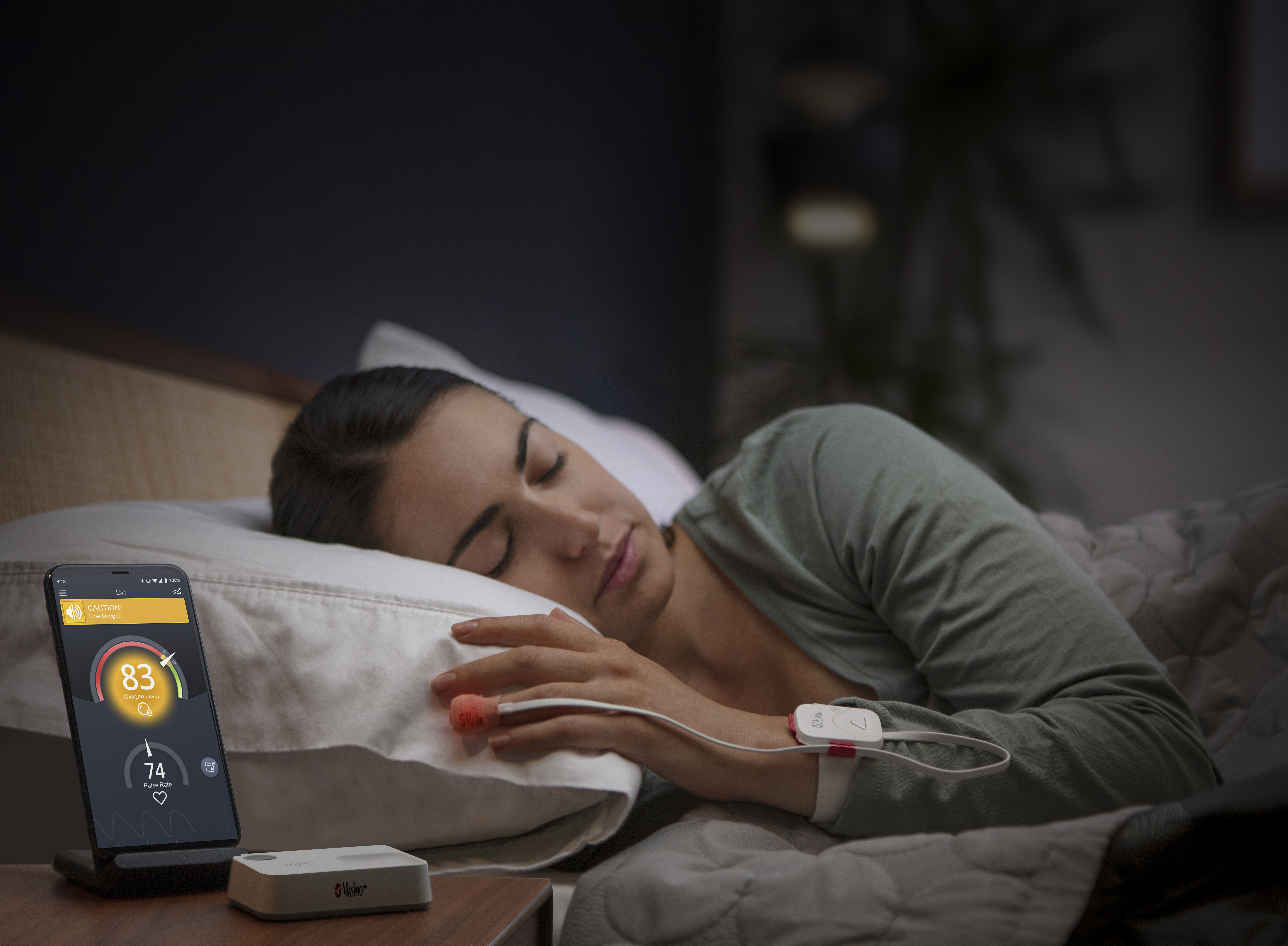 Woman laying in bed next to phone displaying Masimo Safetynet Alert App
